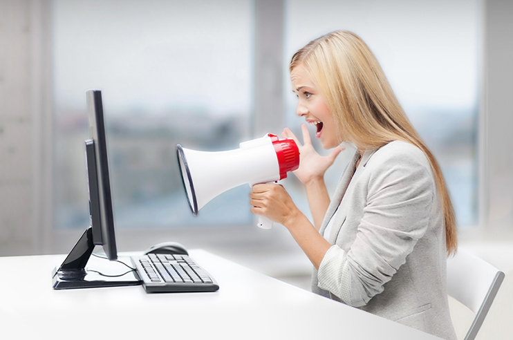Mulher sentada em frente a um computador com um megafone na mão.